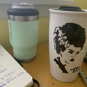 caffeine powered writing: yellow desk with handwritten journal on left, Diet Coke center, and bride of frankenstein coffee mug far right